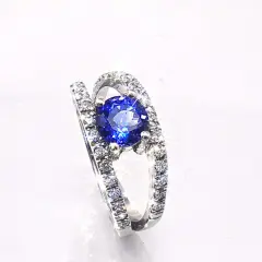 A luxurious Platinum ring featuring a vivid round vivid blue Tanzanite held by four prongs. The split band is adorned with rows of sparkling diamonds.