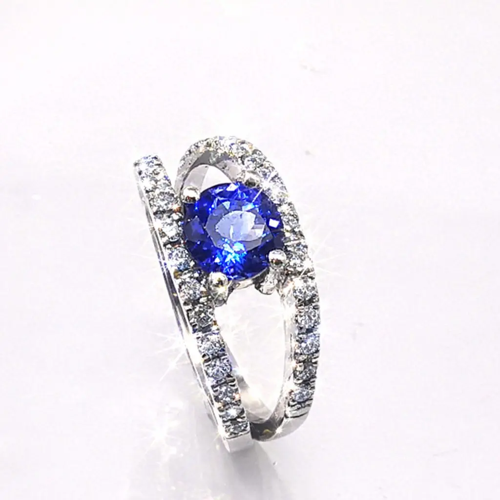 A luxurious Platinum ring featuring a vivid round vivid blue Tanzanite held by four prongs. The split band is adorned with rows of sparkling diamonds.