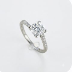Elegant 9ct white gold engagement ring featuring a brilliant round cubic zirconia center stone in a four-claw setting, complemented by pave-set cubic zirconia accent stones along the delicate band.