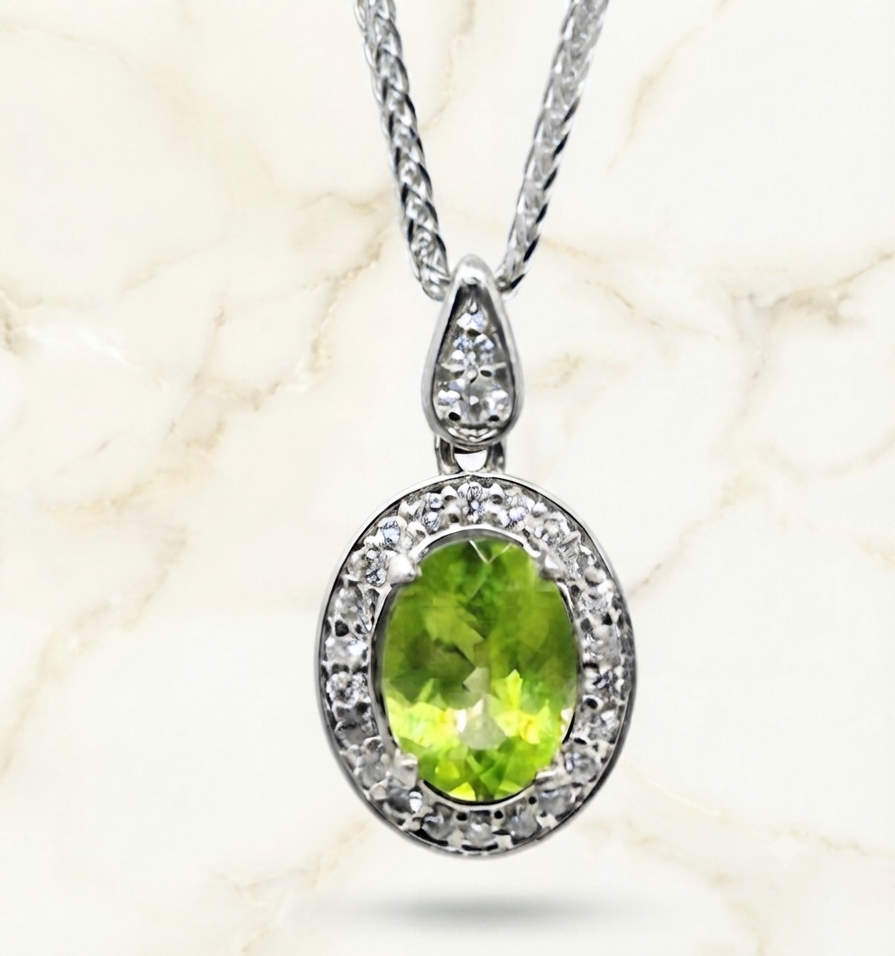 A 9ct White Gold pendant features a vibrant oval-cut green peridot gemstone at its center, surrounded by a halo of