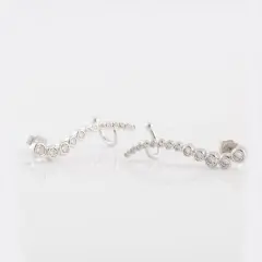 A pair of silver ear climber earrings featuring a curved row of bezel-set cubic Zirconia stones.