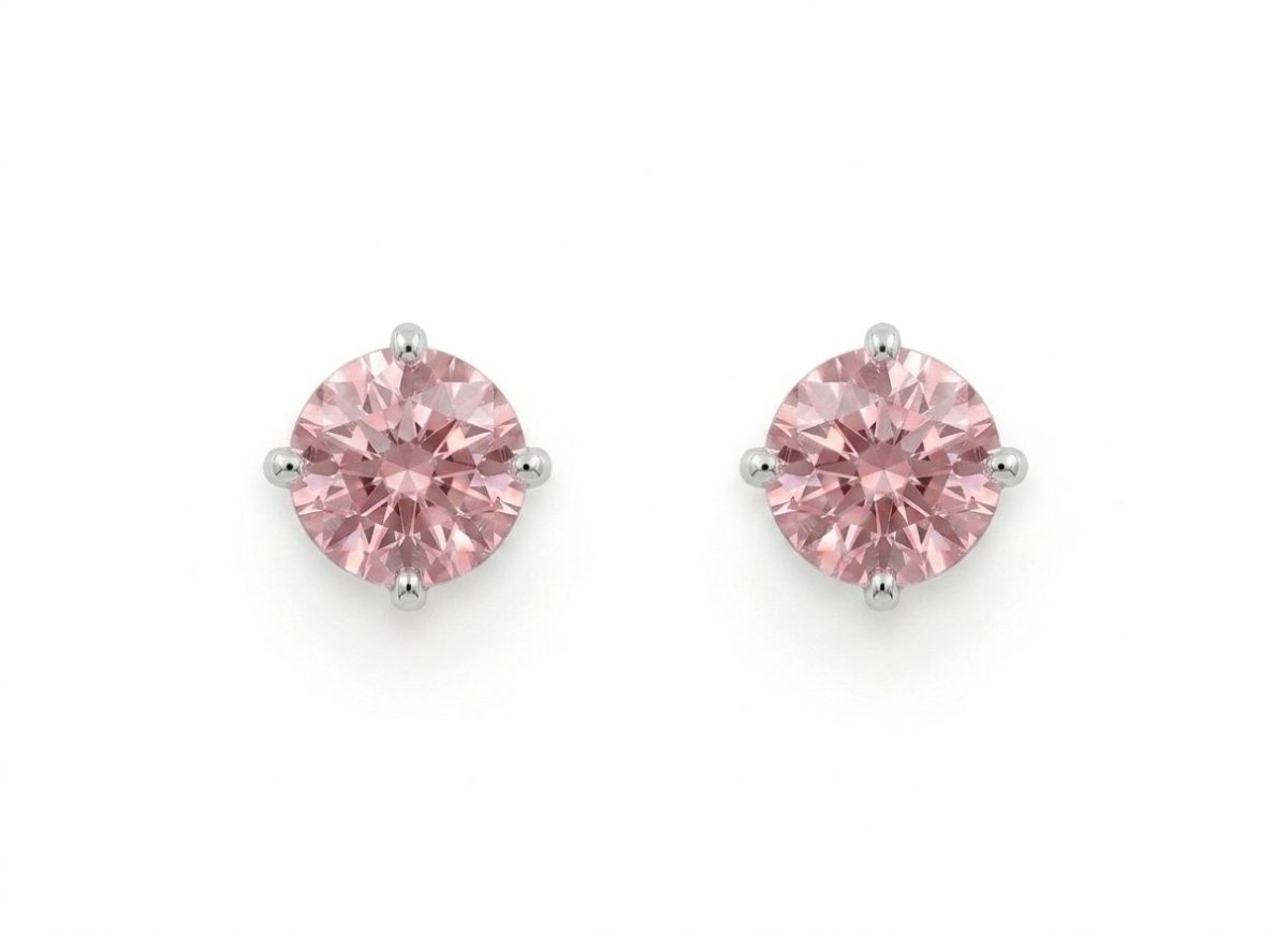 A pair of delicate, round-cut pink sapphire stud earrings set in high-polish white gold claw settings, featuring a soft "alt rosa" pink hue and brilliant facets.