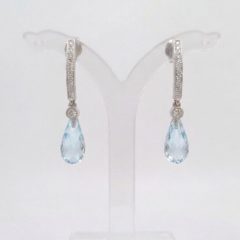 A pair of 9ct White Gold earrings featuring a row of small diamonds on an arched bar, with a bezel-set diamond und a faceted blue topaz briolette teardrop pendant hanging from each.