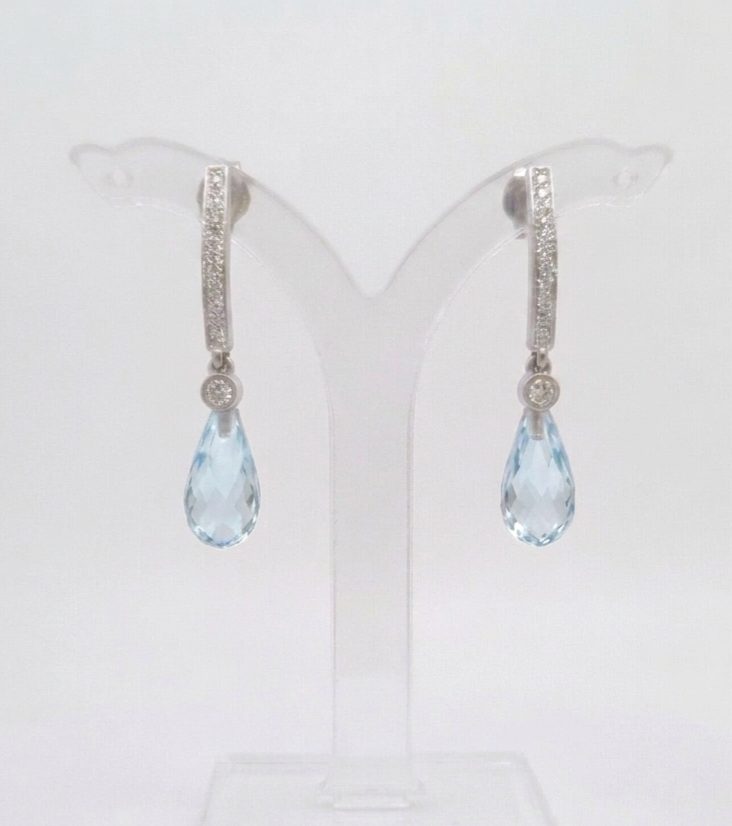 Fida A pair of 9ct White Gold earrings featuring a row of small diamonds on an arched bar, with a bezel-set diamond und a faceted blue topaz briolette teardrop pendant hanging from each.