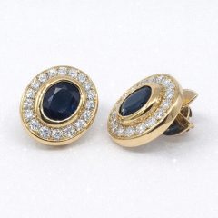 Pair of luxurious 18k yellow gold stud earrings featuring deep blue oval sapphires of 4.0ct totaling encircled by a halo of 32 sparkling round-cut diamonds of 1.28ct.