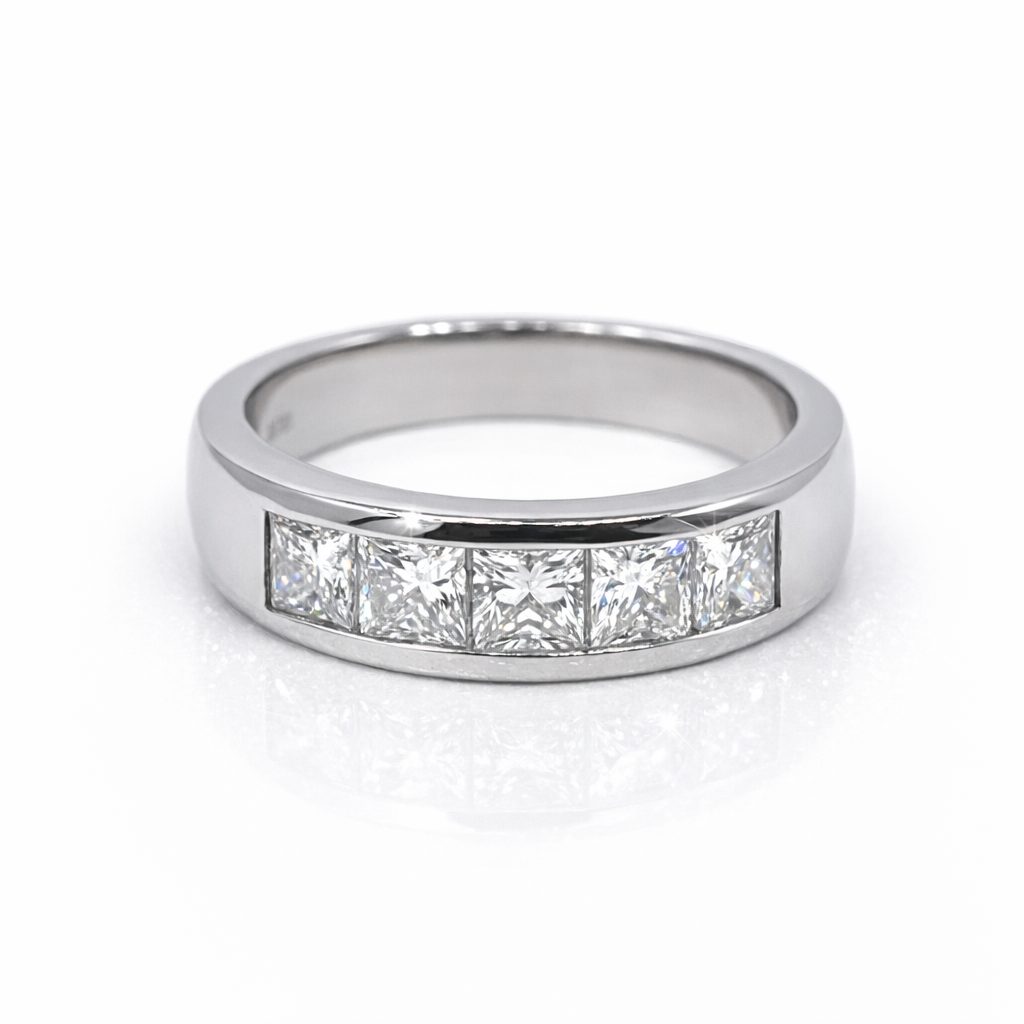 Platinum channel‑set ring featuring five princess‑cut diamonds arranged in a seamless row, photographed against a pure white background. The polished platinum band reflects soft light, while each diamond catches a crisp sparkle, showcasing precision craftsmanship and modern elegance.