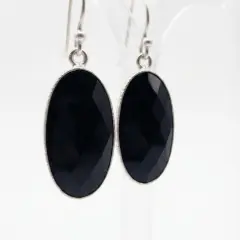 A pair of silver oval earrings with black checkerboard-cut onyx stones on Sheppard hooks.
