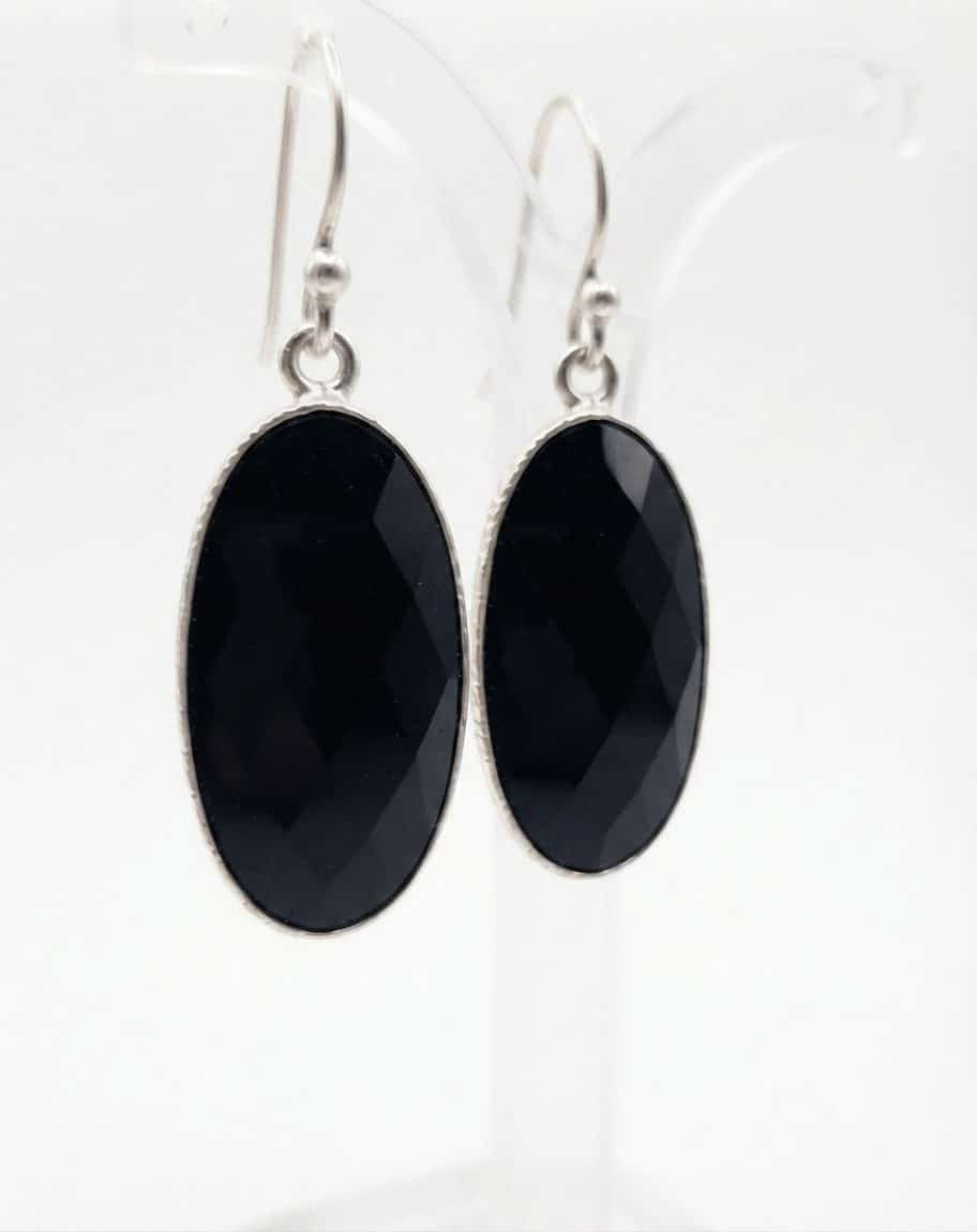 A pair of silver oval earrings with black checkerboard-cut onyx stones on Sheppard hooks.
