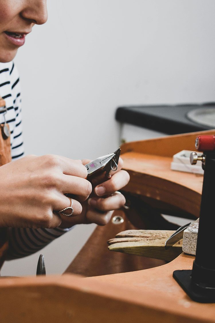 A jeweller's hands inspecting a finished piece of bespoke jewellery in a professional setting.