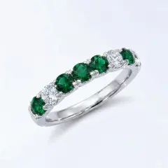 A detailed product of a white gold eternity band set with round green Tourmalines and wound diamonds. The stones are arranged in an alternating pattern with larger 3 Tourmalines in the center.