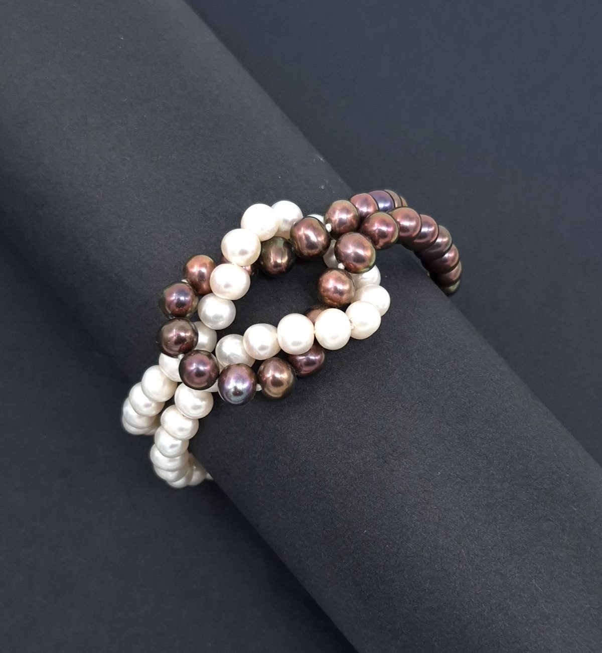 Two interlocking strands of freshwater pearls-one white and one iridescent deep mauve-wrapped around a matte black cylindrical display. Fastened with a magnetic sliding clasp.