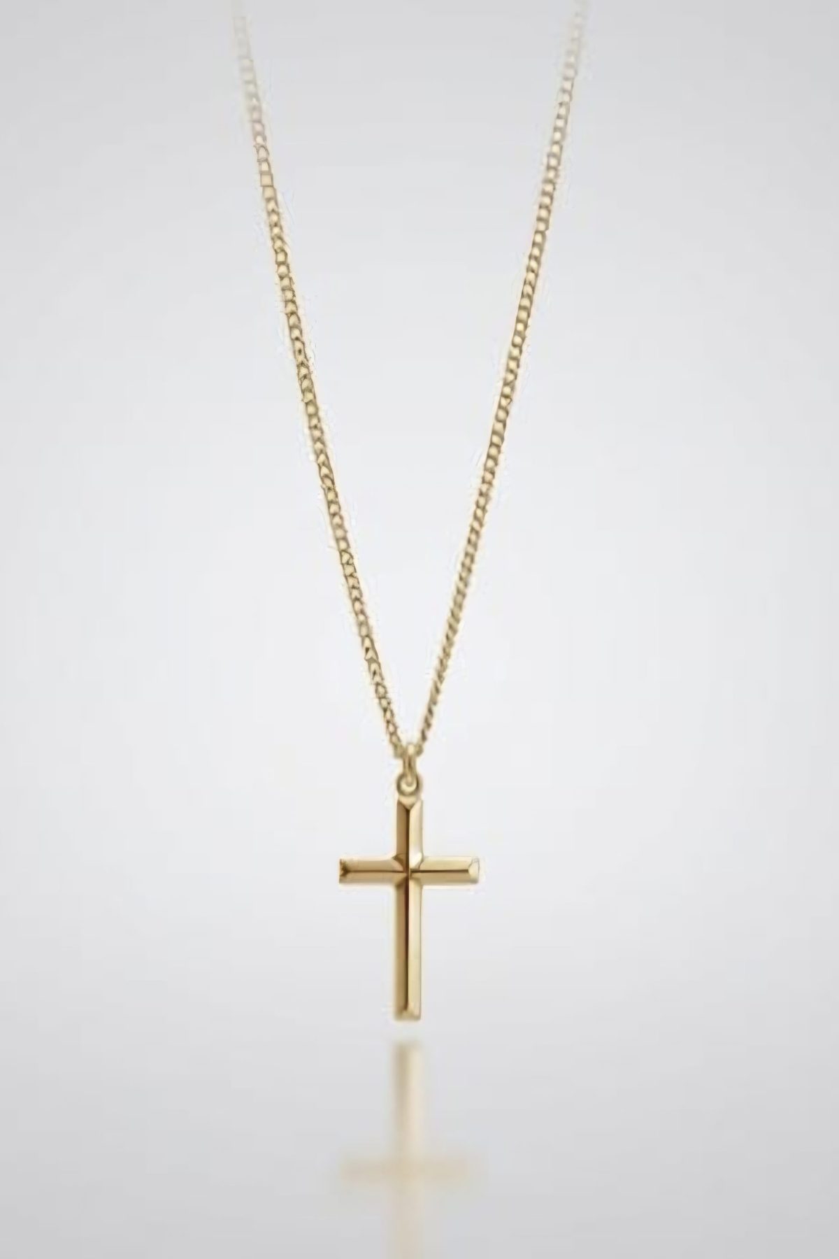 9ct Gold cross pendant necklace with a polished finish on a fine link chain, displayed against a soft grey gradient background