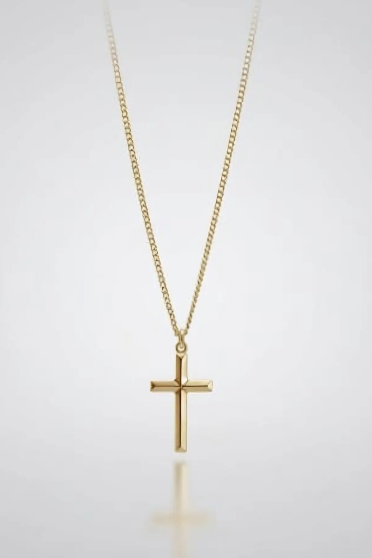 9ct Gold cross pendant necklace with a polished finish on a fine link chain, displayed against a soft grey gradient background