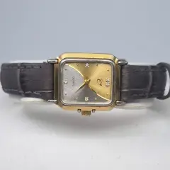 A preloved lady's wristwatch of vintage-style with a rectangular, two-tone gold and silver-finish case. The watch face features a unique diagonal split design, textured with a sunburst pattern in silver on the left and gold on the right. It is accented with small diamond-like hour markers and elegant gold hands. The watch is paired with a textured, dark charcoal-grey leather strap.