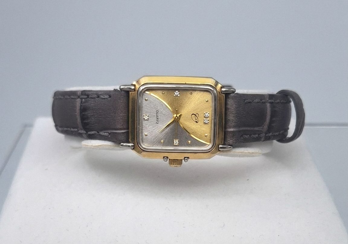 A preloved lady's wristwatch of vintage-style with a rectangular, two-tone gold and silver-finish case. The watch face features a unique diagonal split design, textured with a sunburst pattern in silver on the left and gold on the right. It is accented with small diamond-like hour markers and elegant gold hands. The watch is paired with a textured, dark charcoal-grey leather strap.