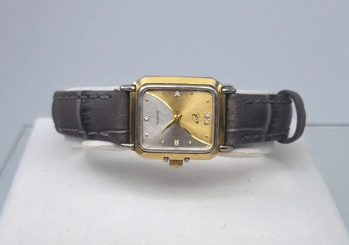 A preloved lady's wristwatch of vintage-style with a rectangular, two-tone gold and silver-finish case. The watch face features a unique diagonal split design, textured with a sunburst pattern in silver on the left and gold on the right. It is accented with small diamond-like hour markers and elegant gold hands. The watch is paired with a textured, dark charcoal-grey leather strap.