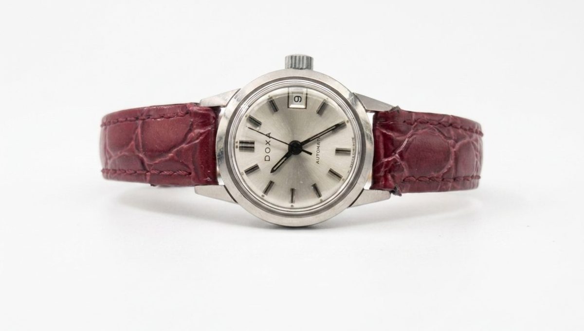 Vintage Doxa ladies automatic watch with a silver sunburst dial, date window, and maroon croc-embossed leather strap.