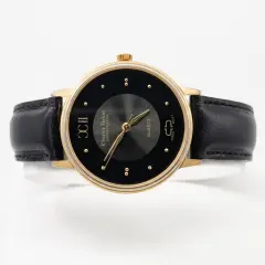 Charles Delon Sophistication men's quartz watch with a round gold-tone case, a minimalist black dial featuring gold stud hour markers and Roman numerals at the 9 o'clock position, paired with a classic black leather strap.