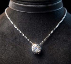A sparkling round-cut diamond solitaire pendant on a delicate gold chain, held in classic tube slider setting.