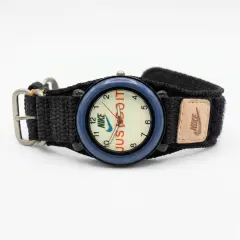 A Nike analog watch featuring a blue bezel and a black fabric strap. The watch face has a beige background with NIKE logo and the text "JUST DO IT" visible, and a small tan-coloured Nake brand patch is attached to the strap.