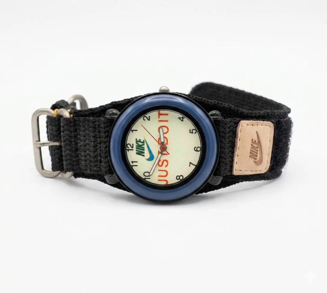 A Nike analog watch featuring a blue bezel and a black fabric strap. The watch face has a beige background with NIKE logo and the text "JUST DO IT" visible, and a small tan-coloured Nake brand patch is attached to the strap.