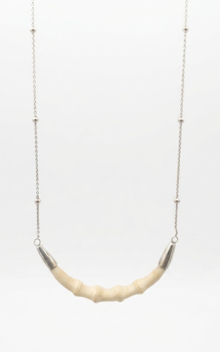 Designer silver necklace featuring a curved, segment-carved bone center piece suspended from a delicate chain with small bead accents.